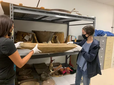 Students lifting a large artifact from a shelf of artifacts