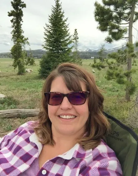 Woman smiling in sunglasses in front of trees and mountains